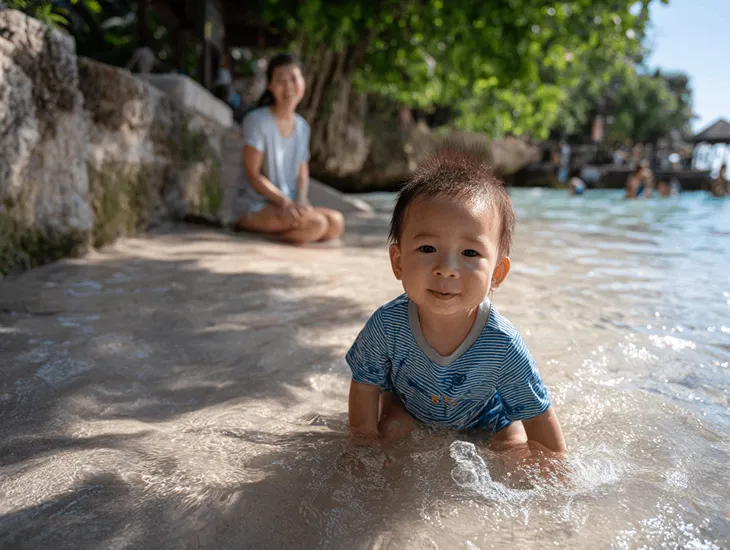 Toddler-friendly beach in Bali 2026 – A parent guiding a young child through ankle-deep water in the protected lagoon area during a calm morning.