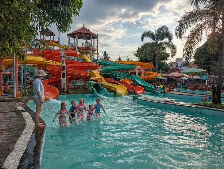 Beachfront stays 2026 – A professional caregiver supervising children playing in a shallow resort pool with water slides.