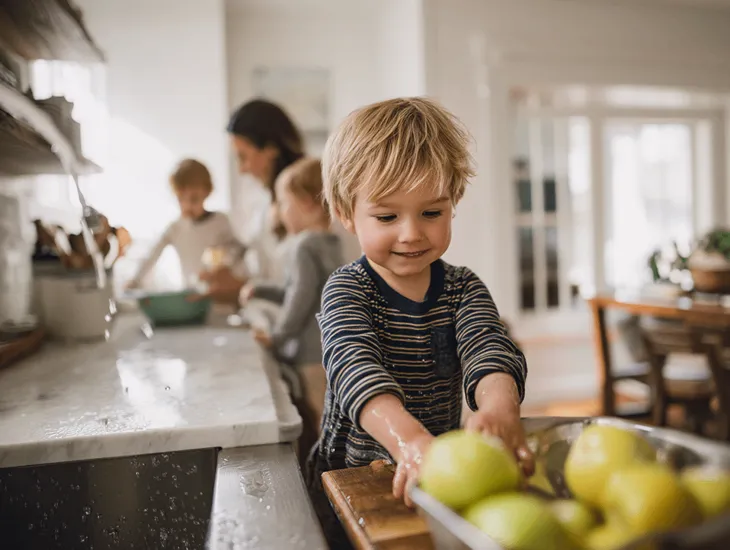 Kitchen safety for kids 2026 – A toddler washing fruit in a sink while a parent supervises from a safe distance