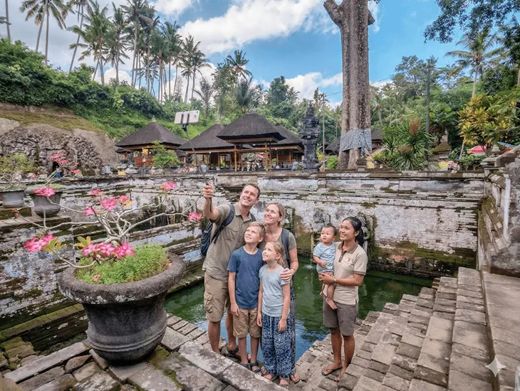 Archaeological site in Indonesia 2026 – A childcare provider in Bali supervising a child near a water goddess statue.
