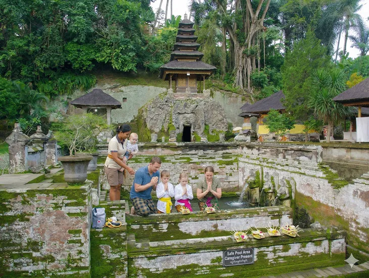 Babysitter in Indonesia 2026 – A professional babysitter in Bali helping a child adjust a sash before entering the cave.