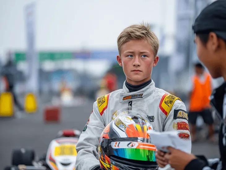 family go-karting in Bali 2026 – A travel assistant helping a teenager adjust a racing helmet and check track telemetry.