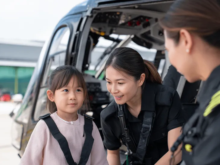 Helicopter Safety Briefing 2026 - A pilot demonstrating the correct use of a seatbelt to a child.