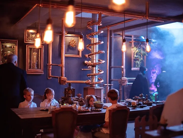 family dinner show in Bali 2026 – A professional makeup artist applying washable green face paint to a child’s cheek in a themed restaurant.