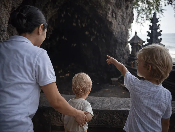 Goa Lawah Temple 2026 – A professional Sitter adjusting a child's sarong near the entrance booth.