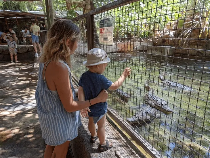 Reptile Park for Kids in Bali 2026 – A babysitter holding a toddler's hand while observing a crocodile feeding session.