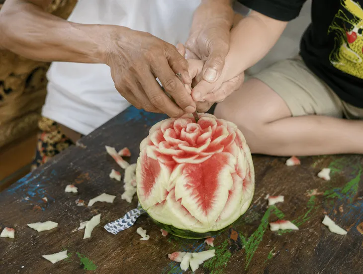 Bali Art Workshop 2026 – Babysitter in Bali helping a student carve tropical fruit patterns carefully