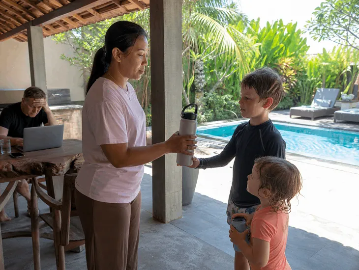 Childcare in Bali 2026. Babysitter helping expat kids stay hydrated during summer holidays.